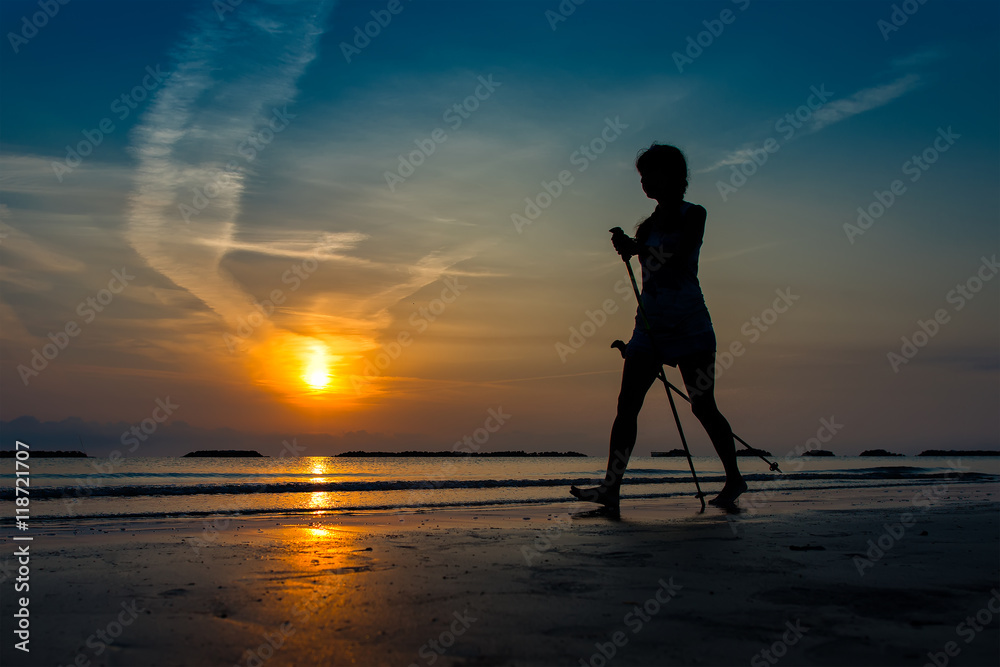 Woman practicing nordic walking in the beach at sunrise in late