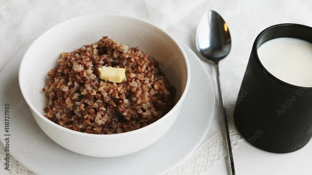 Cooked buckwheat groats with butter and mug of milk on a table. Slow pan. Cooked buckwheat groats with butter and mug of milk on a table. Slow pan.
