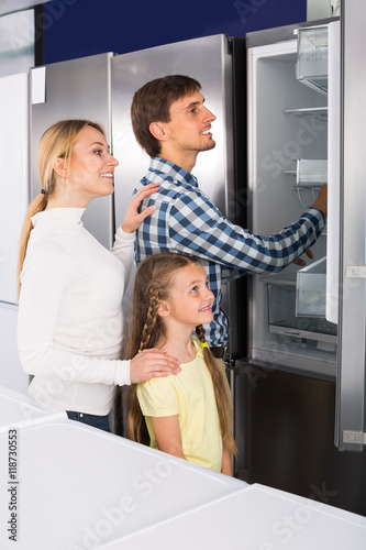 Smiling couple with girl choosing refrigerator
