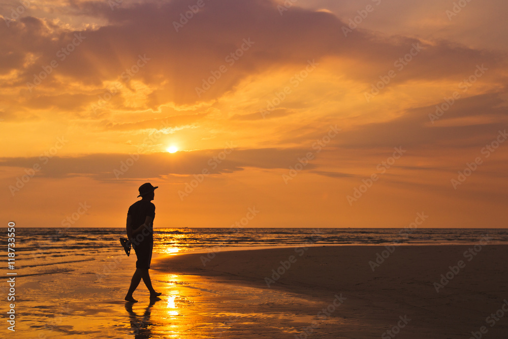 Man walking along the beach at sunset