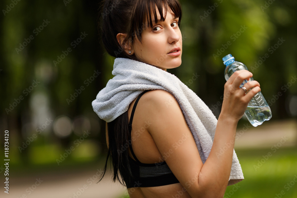 Fitness girl with water bottle and towel on shoulders outdoors Fitness girl with water bottle and towel on shoulders outdoors