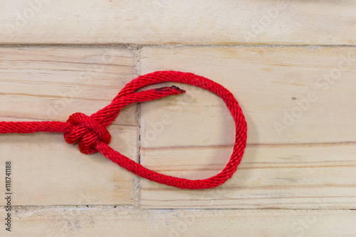 bowline knot made from red synthetic rope, tightening on wooden background