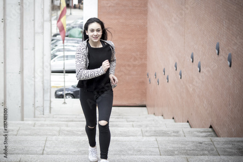 Chica joven morena subiendo y bajando feliz las escaleras en la ciudad. Modelo morena posando en las escaleras.