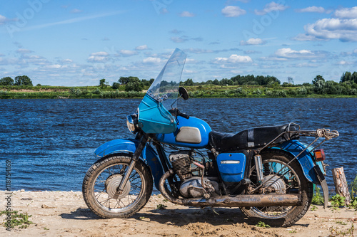 Old blue motorbike stand near the Oka river. 