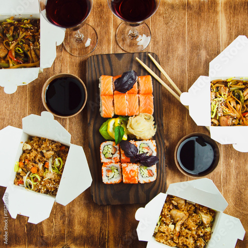  Bowl of stir fried udon noodles garnished with black sesame seeds and fresh mint with wooden chopsticks, sushi and glasses wine. Dinner s Japanese restaurant photo