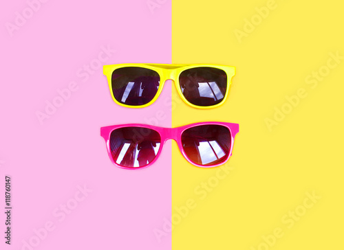 Two sunglasses yellow pink over a colorful background