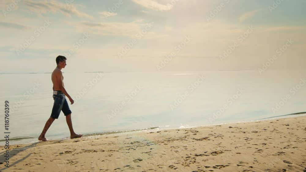 Teenager boy walking along the beach at sunset. Against the backdrop of the beautiful evening sky Teenager boy walking along the beach at sunset. Against the backdrop of the beautiful evening sky