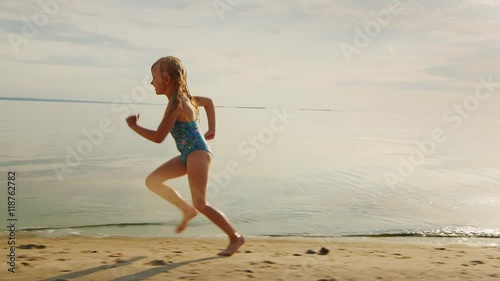 Carefree blonde girl 5 years runs along the shore. He laughs off her feet flying a lot of water splashing photo