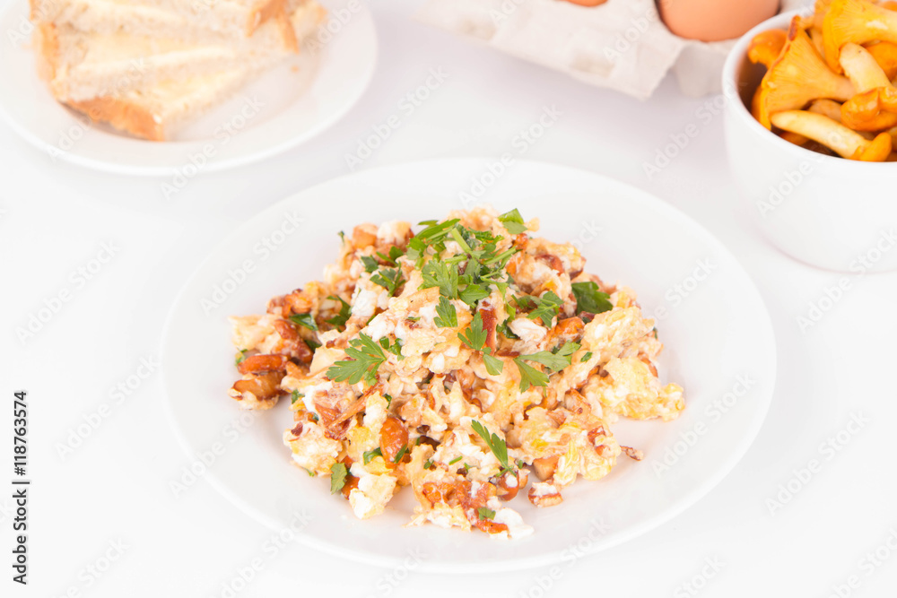 Scrambled eggs with chanterelle and parsley with some white bread on a white background