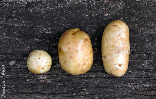 Three raw potatoes of different shapes on an old black wooden plank. view from above close-up photo