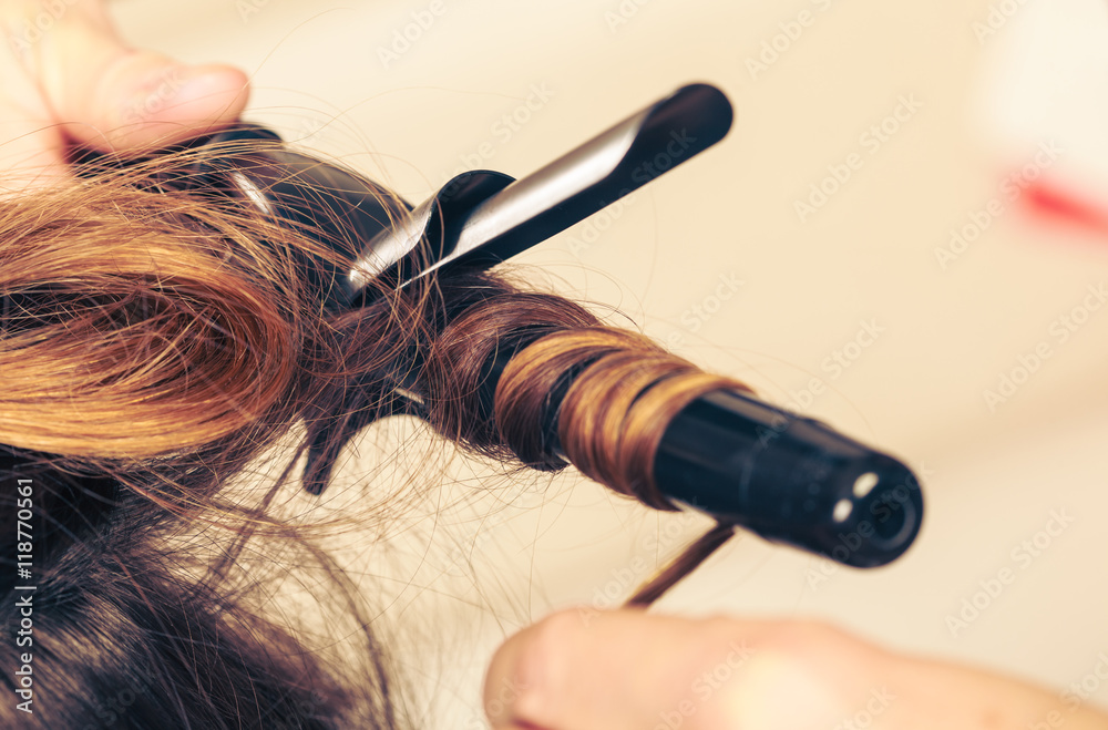 Naklejka premium Stylist curling hair for young woman.
