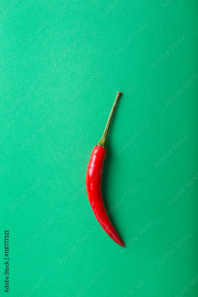 single, red hot chili pepper isolated on green paper background, vertical single, red hot chili pepper isolated on green paper background, vertical