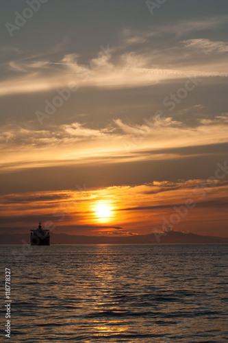 huge cargo ship at golden sunset, beautiful sky and clouds in English Bay, Vancouver, British Columbia, Canada