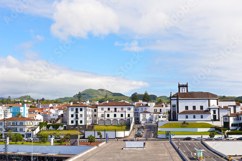 View on Ponta Delgada from the ocean pier, Azores, Portugal. White houses with colorful tiled roofs and countryside with mountain ridge on the horizon. © avmedved