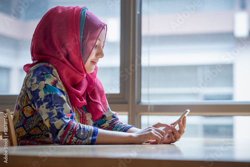 Muslim woman holding and working with mobile phone.