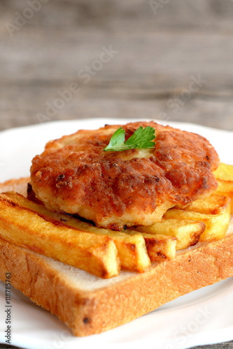 Sandwich with fried potatoes and Turkey meat cutlet on a plate and on old wooden table. A sandwich cooked from white bread, fried potatoes and Turkey burger. Closeup 