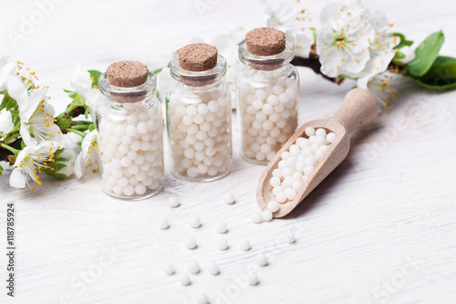 homeopathic pills with spring flowers on white wooden background