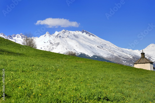 chapelle dans prairie verdoyante aux pieds des montagnes enneigées