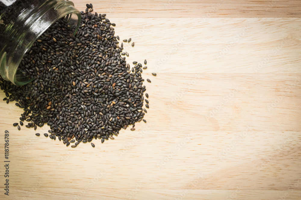 Black sesame spilled out on wooden background; Food background with copyspace Black sesame spilled out on wooden background; Food background with copyspace