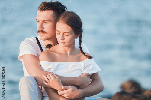 Happy young romantic couple relaxing on the beach and watching the sunset