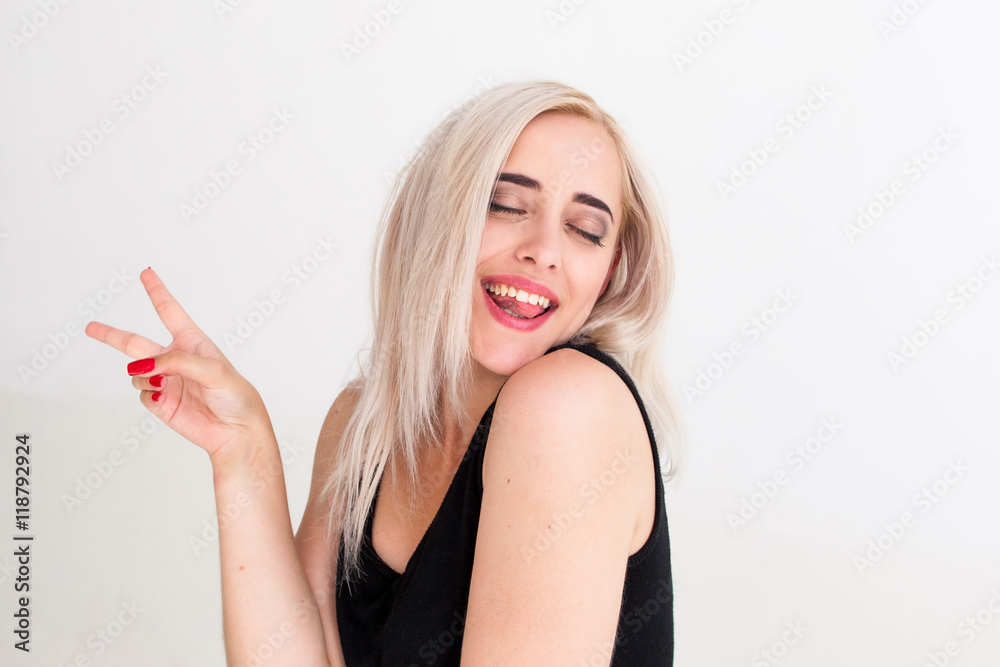 Portrait of cheerful woman with peace hand sign. Drunk playful blonde in black dress with closed eyes laughing and posing jocosely at camera, white background Portrait of cheerful woman with peace hand sign. Drunk playful blonde in black dress with closed eyes laughing and posing jocosely at camera, white background