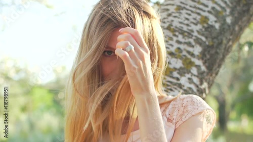 Portrait of beauty young blonde while she sitting on the tree branch, smiling and posing to camera