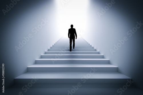 Businessman climbing the stairs towards light.