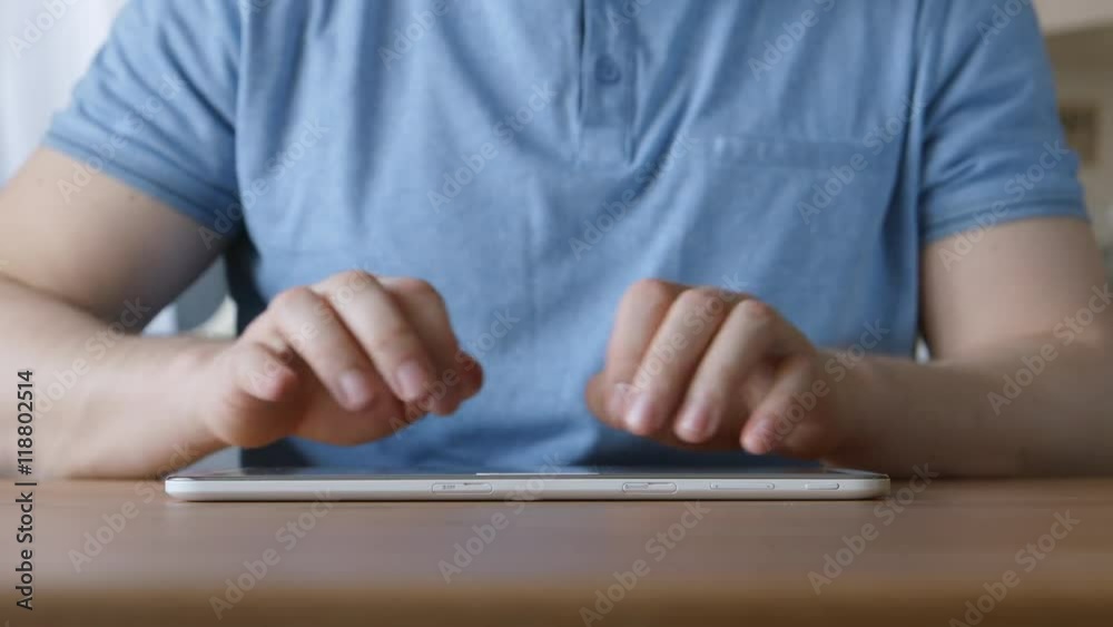 A hands of young man typing on a tablet PC at the table at home A hands of young man typing on a tablet PC at the table at home
