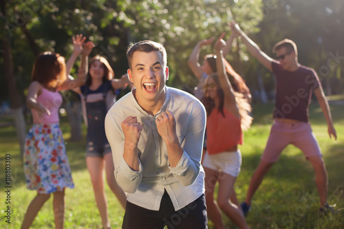 young man celebrating victory while his friends jumping and dancing for joy in the background