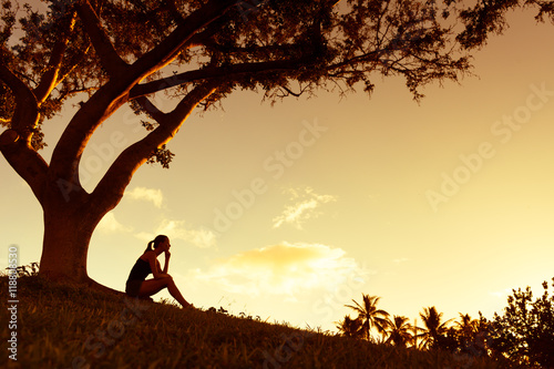 Young woman siting under a tree enjoying the beautiful golden sunset. 