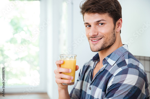 Smiling young man drinking fresh juice on the kitchen
