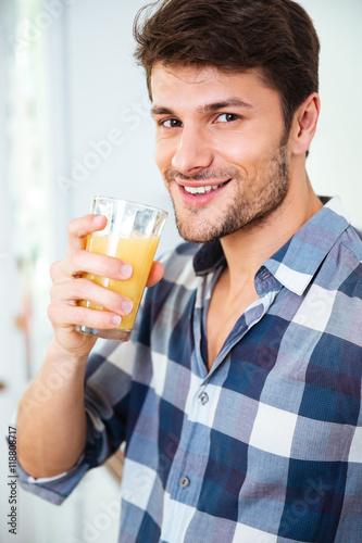 Happy young man in plaid shirt drinking juice at home