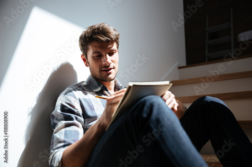 Man sitting on stairs at home and writing in notepad photo