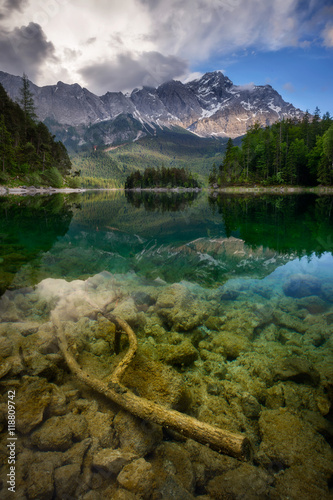 Beautiful reflection of highest mountain peak Zugspitze with old tree under water at Eibsee lake and amazing stormy clouds, Bavaria, Germany.
