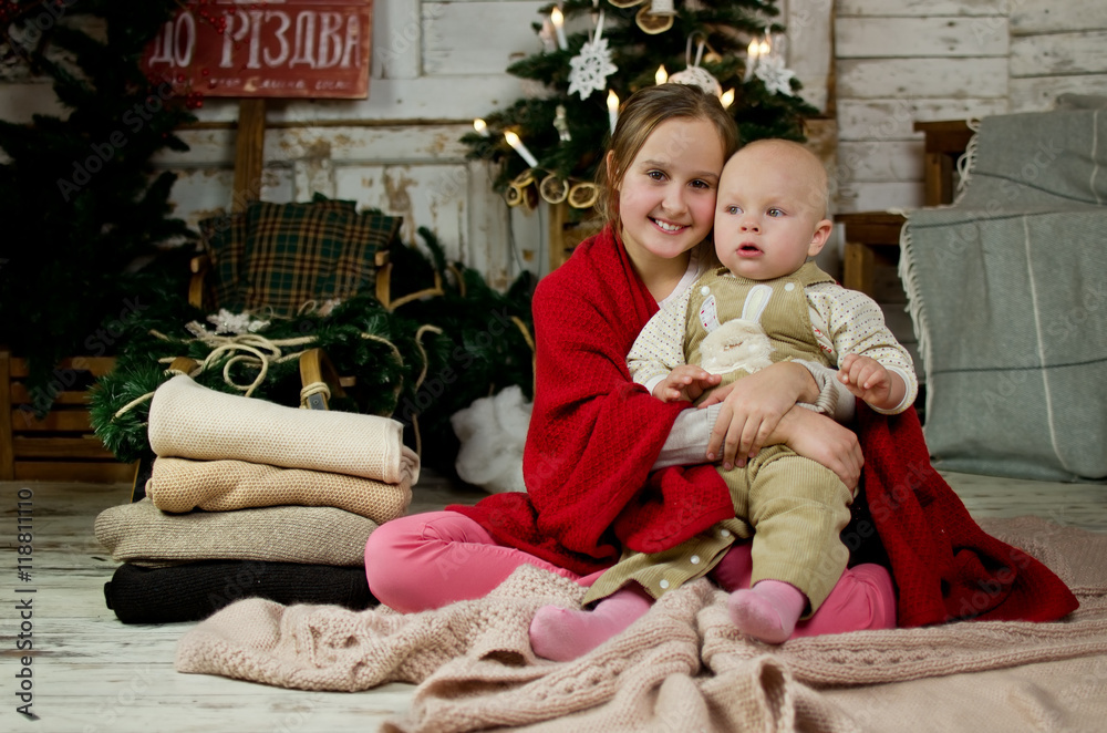 Girl and little brother sitting on a blanket and covered with a blanket