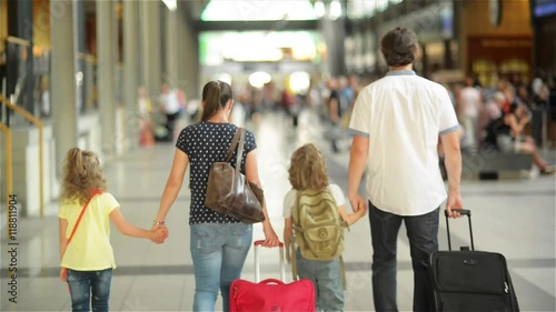 Happy family with little girl and boy going on railway station, mother father and the kids walk through the airport with suitcases