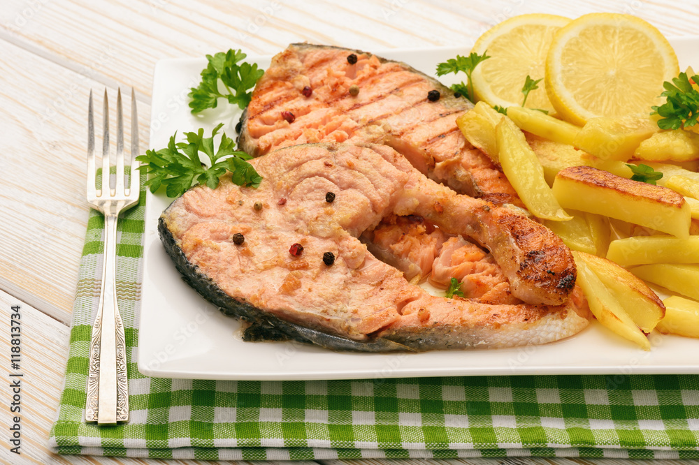 Grilled salmon with fried potatoes and slices of lemon.
