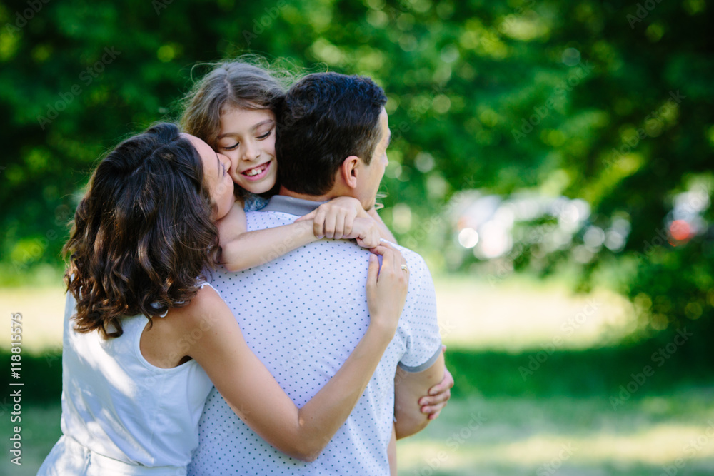 Young happy family three daughter mother and father hug each other in the park Young happy family three daughter mother and father hug each other in the park