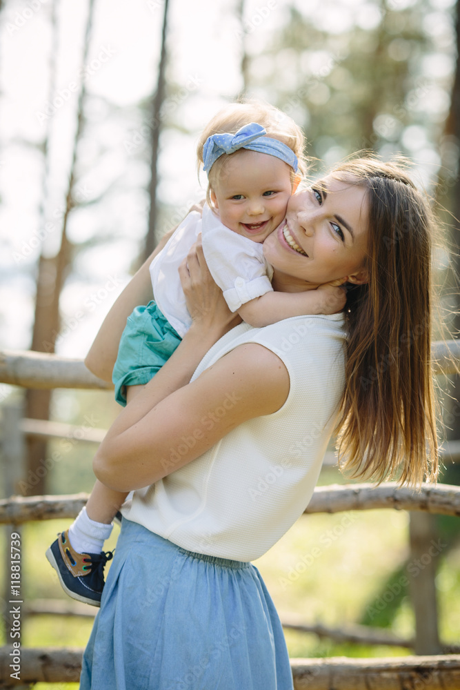 happy mother hug her baby daughter smiling in the green park near forest in sunlight outdoor shot