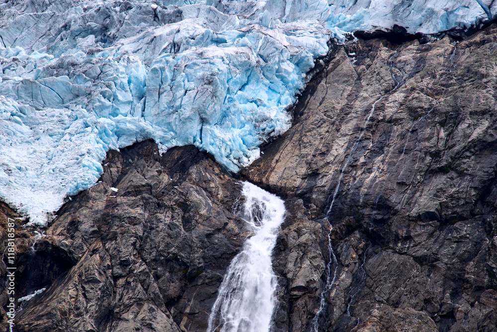 Blue ice and a small waterfall with melted water at the edge of Folgefonna glacier on a mountain side in Norway