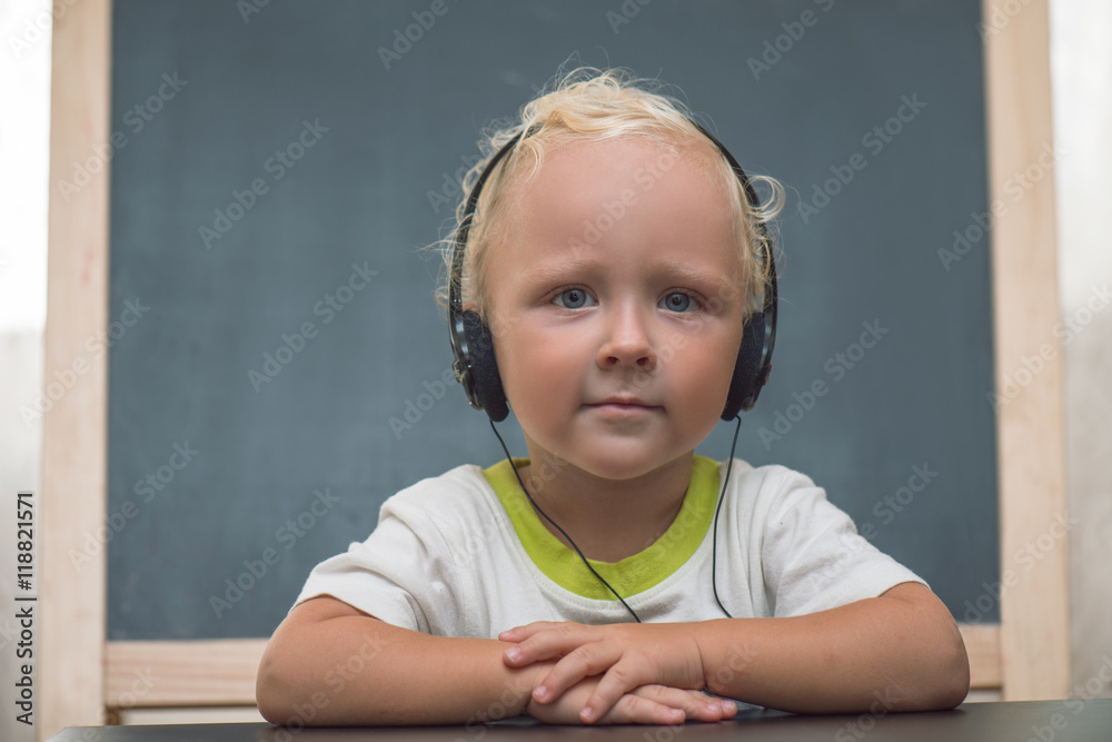Baby with headphones sitting at a table against the background of the easel Baby with headphones sitting at a table against the background of the easel