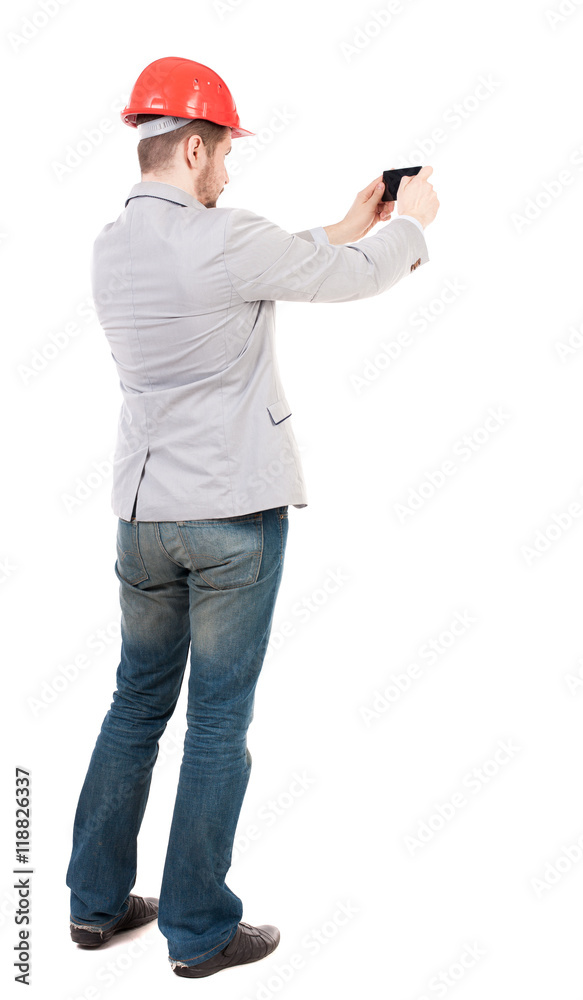 Backview of business man in construction helmet stands and enjoys tablet or using a mobile phone. Standing young guy. Rear view people collection. backside view of person. Isolated over white Backview of business man in construction helmet stands and enjoys tablet or using a mobile phone. Standing young guy. Rear view people collection. backside view of person. Isolated over white