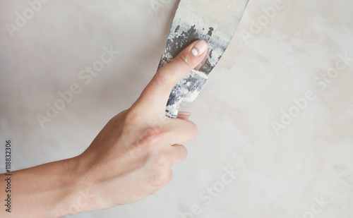 Woman hand with manicure. Closeup of palette-knife or scraper and cement filling for house renovation construction. 