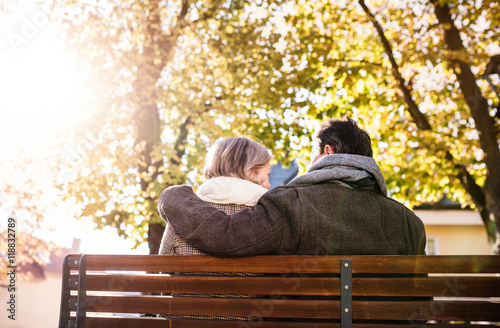 Senior couple sitting on bench, autumn nature. Rear view