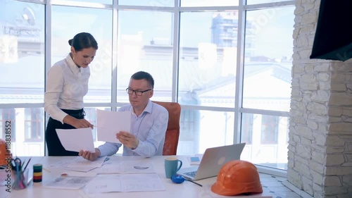 A businessman and businesswoman, engineers working in bright clean office. Discussing the the construction project, plan, drawing, scheme. HD. photo