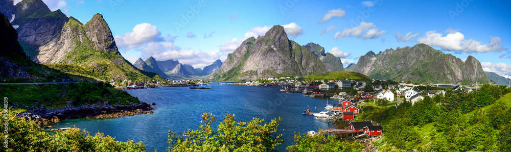 Reine in Lofoten Islands, Norway, with traditional red rorbu huts under blue sky with clouds. 