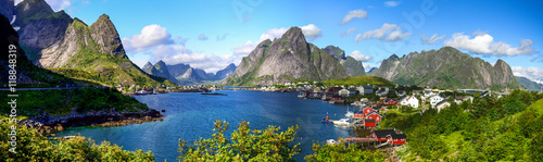 Reine in Lofoten Islands, Norway, with traditional red rorbu huts under blue sky with clouds.  photo