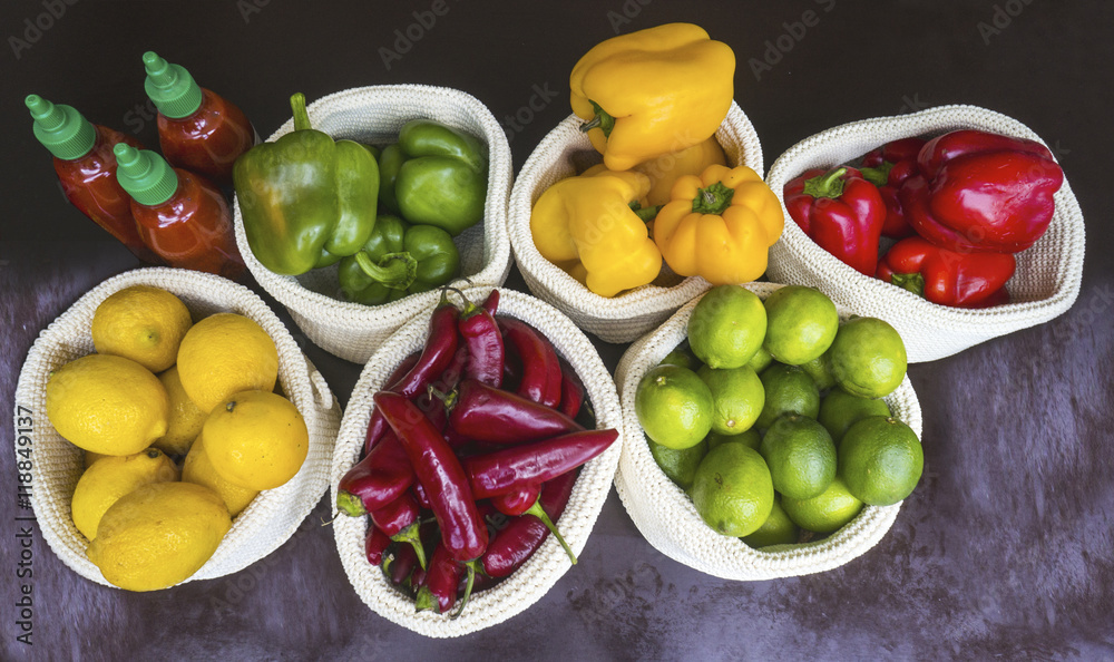 Naklejka czerwona, żółta, zielona papryka, cytryny, chilli, limonki i sos pomidorowy leżą w białych torebkach na ciemnym blacie widok