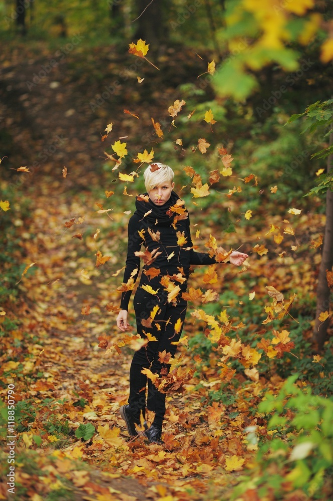 Beautiful girl with falling leaves in the autumn park