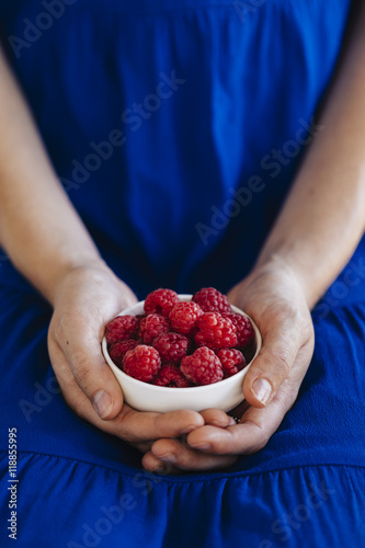 Young woman in blue dress holding a white bowl containing raspberries